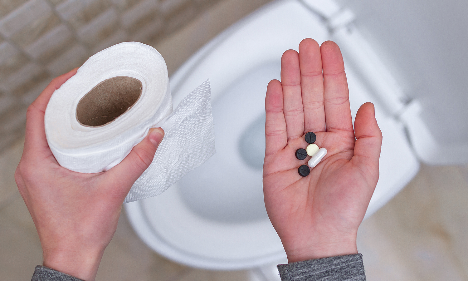 Person hält Toilettenrolle und Abführmittel in Kapselform in der hand