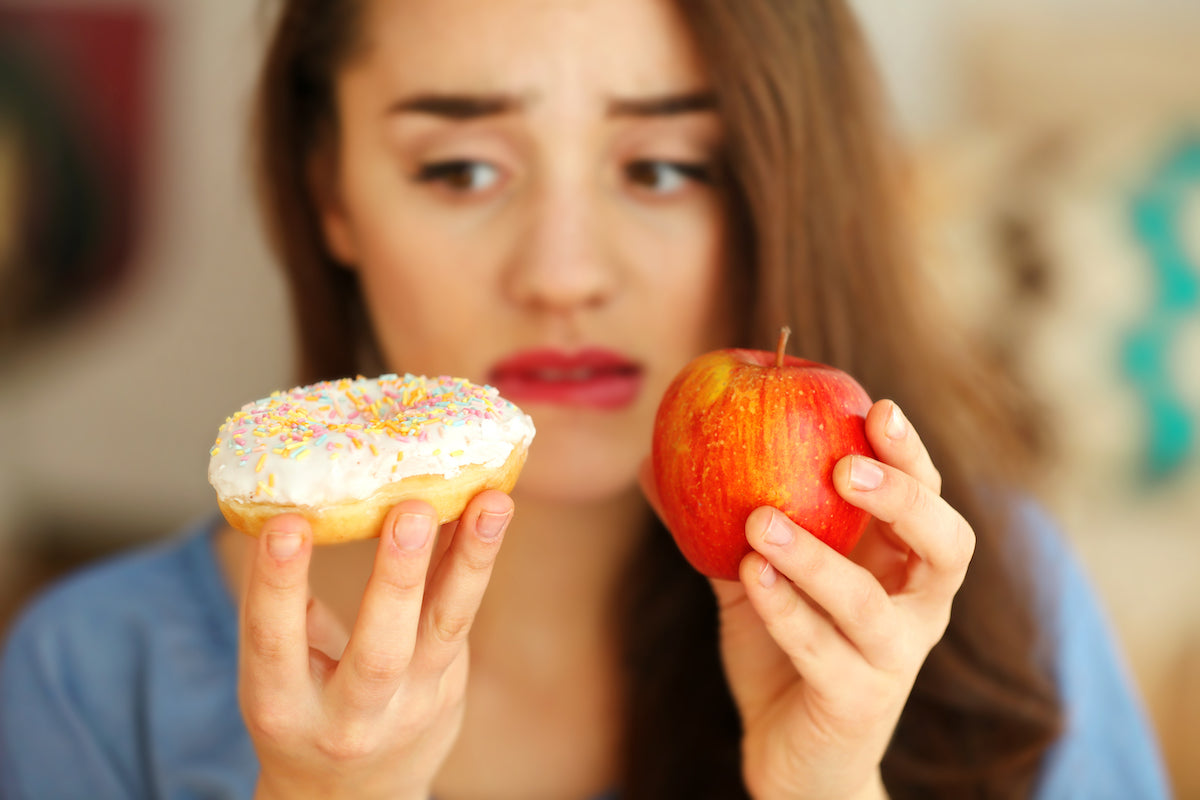 Frau hält Apfel und Donut in den Händen