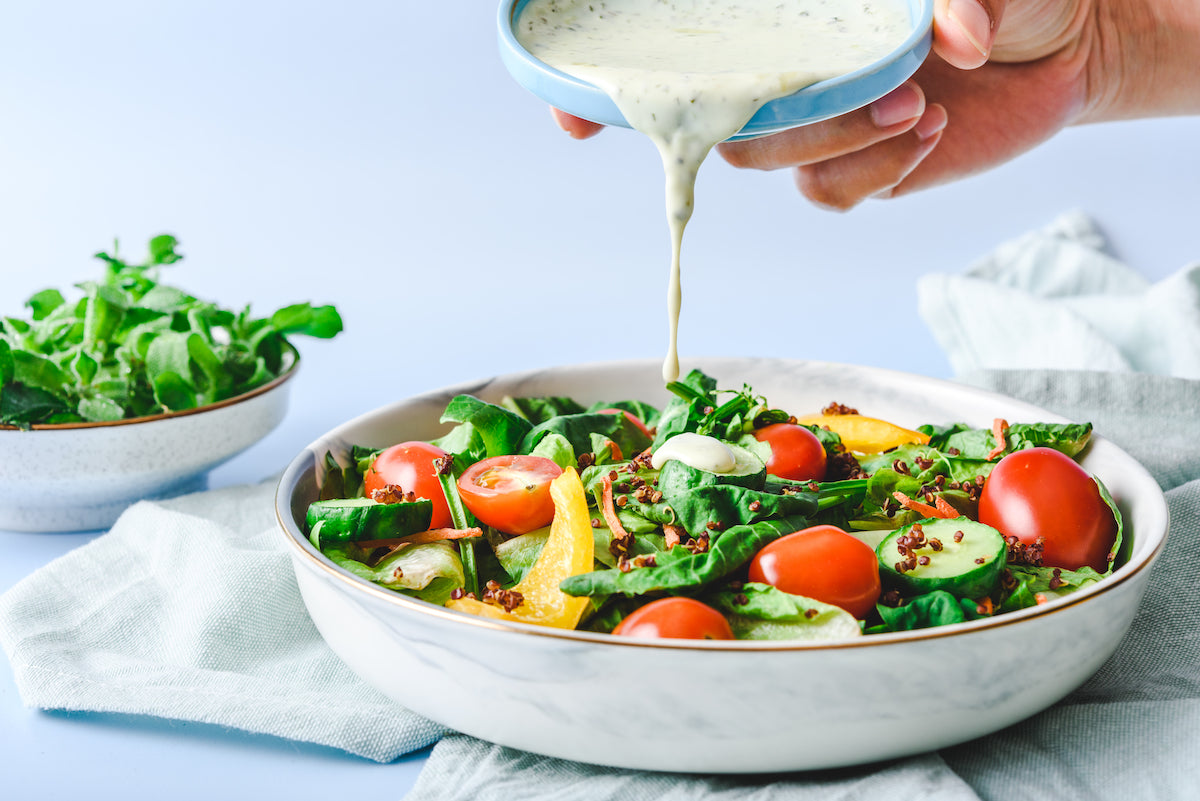 Auf einen Salat wird ein helles Dressing gegeben