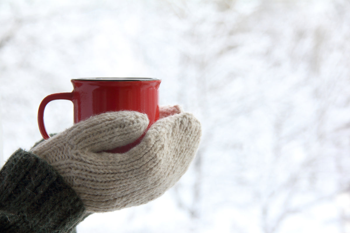 Hände mit Handschuhen halten eine Tasse