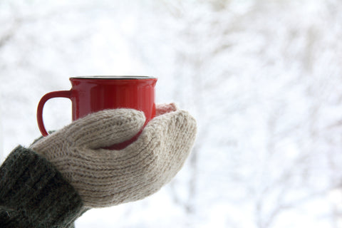 Hände mit Handschuhen halten eine Tasse