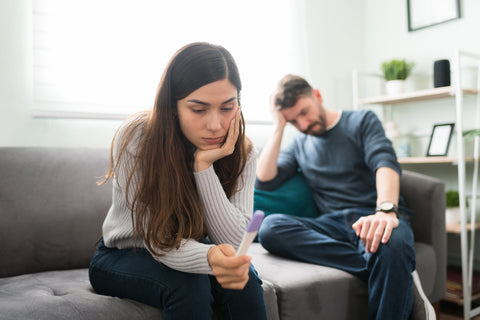 Mann und Frau sitzen auf dem Sofa, die Frau hält einen Schwangerschaftstest in der Hand