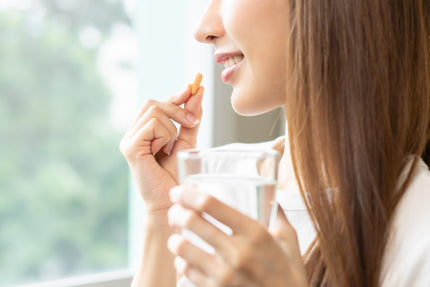 FAQ Multi-Komplex: Frau nimmt eine Kapsel mit Glas Wasser ein