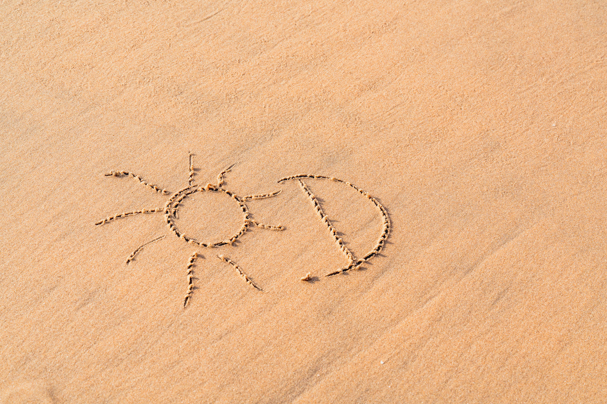 In den Sand geschrieben steht: Vitamin-D, dazu gezeichnet ist eine kleine Sonne