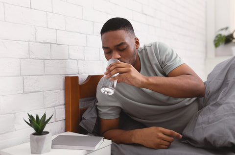 Ein Mann trinkt im Bett liegend ein Glas Wasser