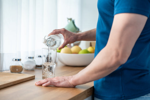 Person gießt ein Glas Wasser ein