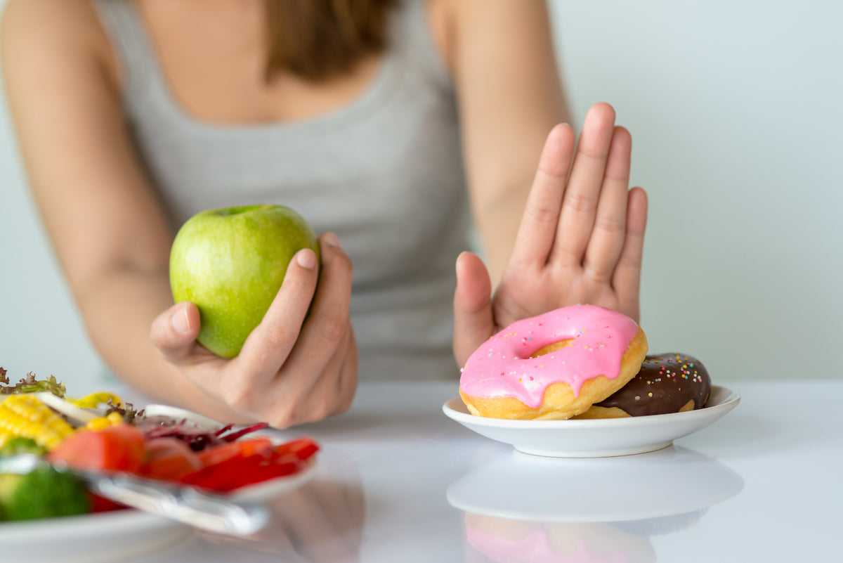 Frau mit Apfel in der Hand lehnt Teller mit Donuts ab