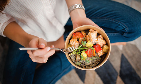 Eine Frau isst eine Bowl mit Paprika und Lachs
